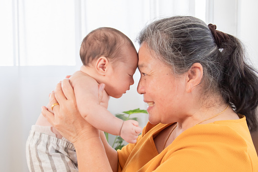 Selective focus grandmother holding in air and touching foreheads with newborn baby, granny expressing understanding candid emotions and love to sweet little child. Happy friendly family concept.