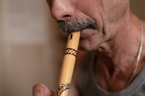 senior man playing the flute. faceless unprofessional male of elderly caucasian recorder people with a moustache with mouth and lips play on pipe amateur music close up at home. hobbies and leisure