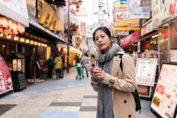 istock lost Asian Korean woman visitor using navigation app on cellphone and looking into space checking for direction while visiting Shinsekai food street in Osaka Japan 1436900308