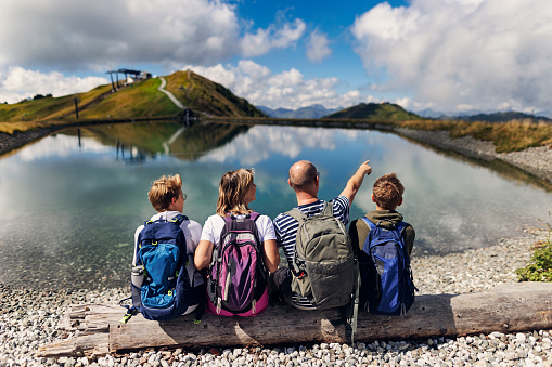 Family is hiking in the Alps - Salzburg, Austria. They are sitting on a bench high in the mountains and looking at the view and the lake.\nCanon R5