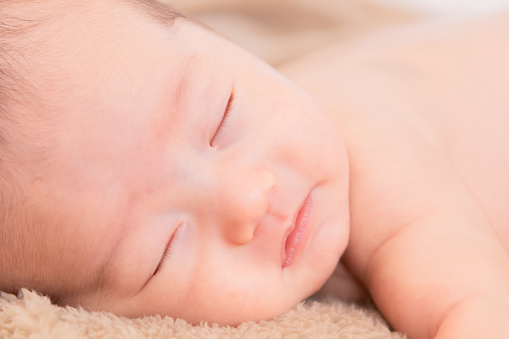 Close up Asian newborn baby sleeping peacefully on beige blanket at home, adorable infant sleep in dream. Little toddler 1-2 month lying on bed with safe. Family morning at home,Children hygiene.