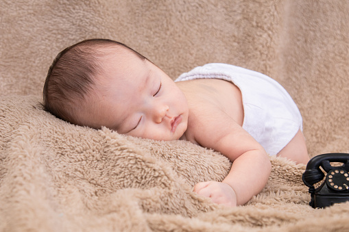 Asian newborn baby sleeping peacefully in brown blanket at home, adorable infant sleep in dream. Little toddler 1-2 month lying on his stomach with safe. Family morning at home,Children hygiene.