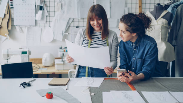 istock Young women working in design industry are comparing sketches and talking about them while working in modern tailor shop. Productive teamwork concept. 1436905688