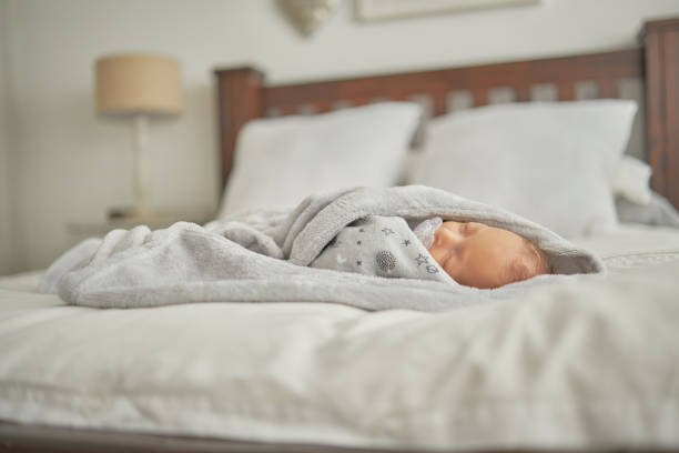 Newborn, sleeping and baby in blanket on bed cute, adorable and sweet moment. Sleep, peace and quiet for young child taking a nap in bedroom. Love, infant care and newborn baby asleep in family home stock photo