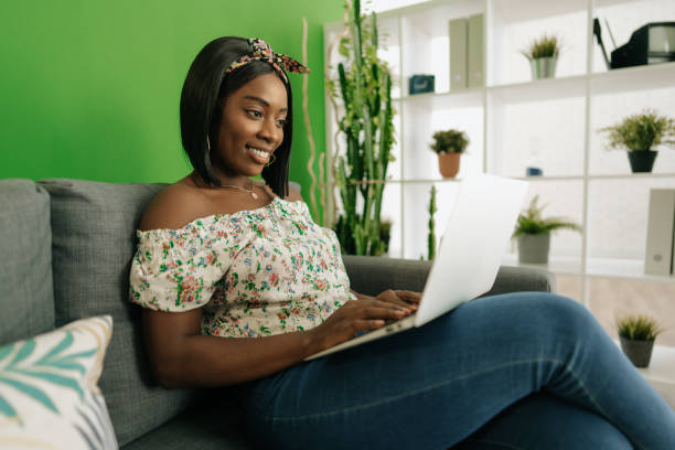 istock Young african woman working on laptop computer at home sitting on sofa. 1436909024