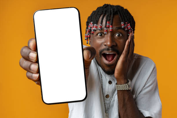 istock Excited young african man holding smartphone with white blank screen in hand on yellow studio background 1436909058