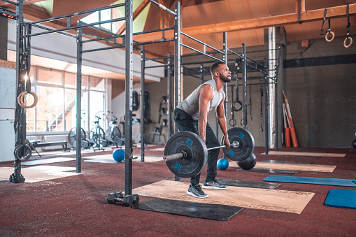 Bearded male athlete practicing deadlift with barbell at health club. Man is exercising with weights. He is training at gym.