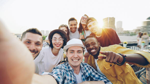 istock Handsome young man in cap is looking at camera to take selfie, people are having fun, making funny faces and gestures and laughing. 1436909153