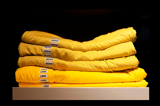 A Close-up of a stack of yellow t-shirts with large and medium stickers isolated on black background