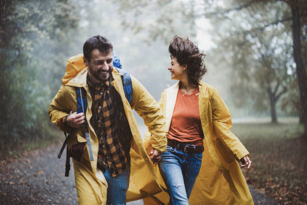 istock Cheerful couple in yellow raincoats having fun while running on rain in forest. 1436912862