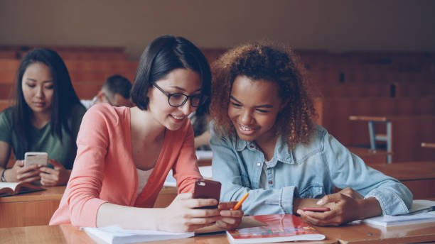 istock Pretty girls students are using smartphone, watching screen, talking and laughing sitting at desks at university. Social media, internet, millennials and education concept. 1436912977