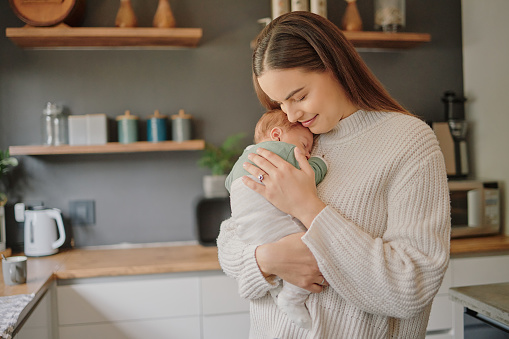 Love, happy and mother with baby in kitchen together and hug for family, relax and growth in the morning. Lifestyle, peace and wellness with mom and sleeping newborn for nursing, care and health