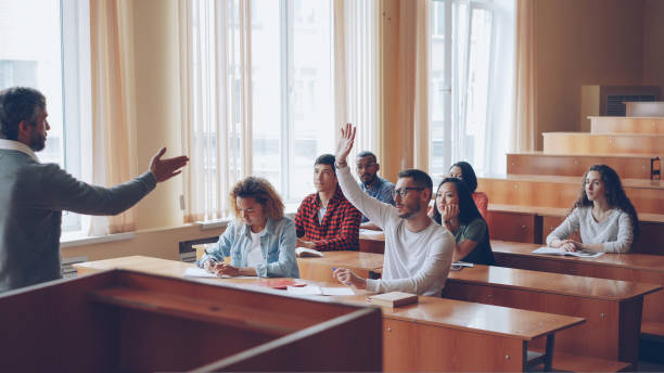 istock Smart guy student is raising hand and talking to professor while fellow students are listening to them and smiling. Pupil and teacher relations concept. 1436914615
