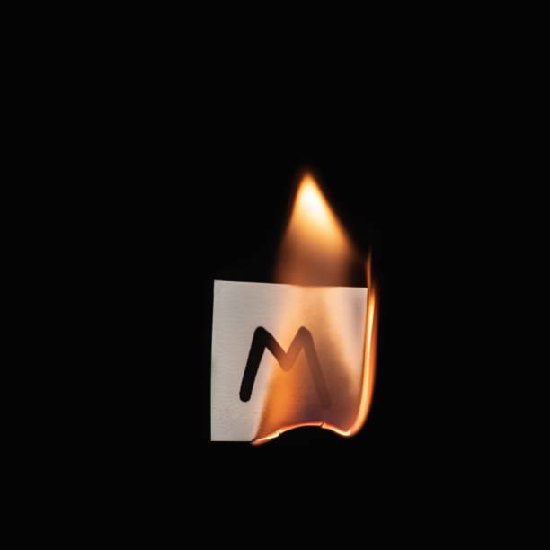 istock Small paper with letter M burning on a black background 1436916682