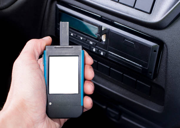 A close-up shot of a driver's hand holding a digital tachograph reader with blank white screen