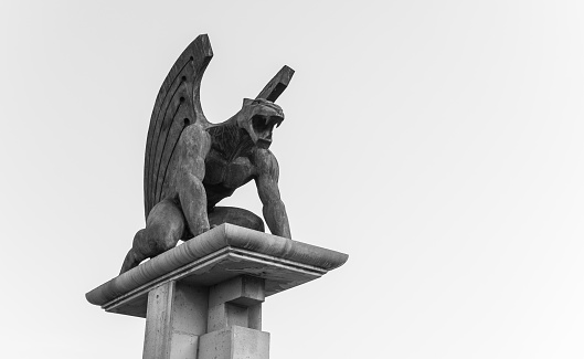 A low angle grayscale shot of a Gargoyle statue under a cloudy sky
