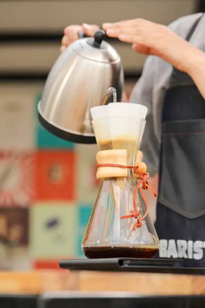 A vertical shot of a barista pouring water in a pour-over style coffeemaker on a food weight scale