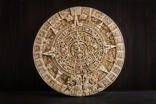 A round engraved stone with Aztec calendar on a wooden background