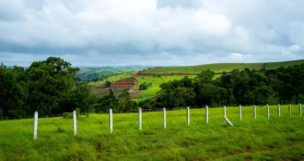 Photo of Landscape with green field and fenced area under cloudy sky in Mondulkiri province in Cambodia