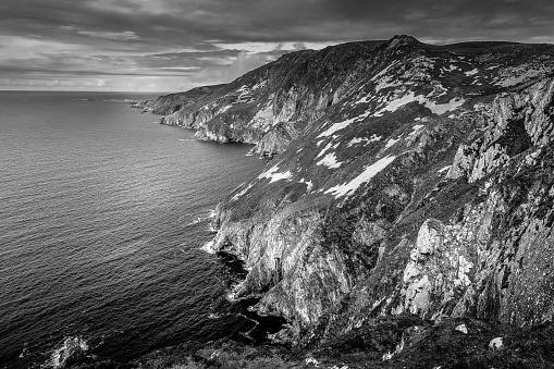 A black and white landscape of sea and rocks under a cloudy sky in Ireland.