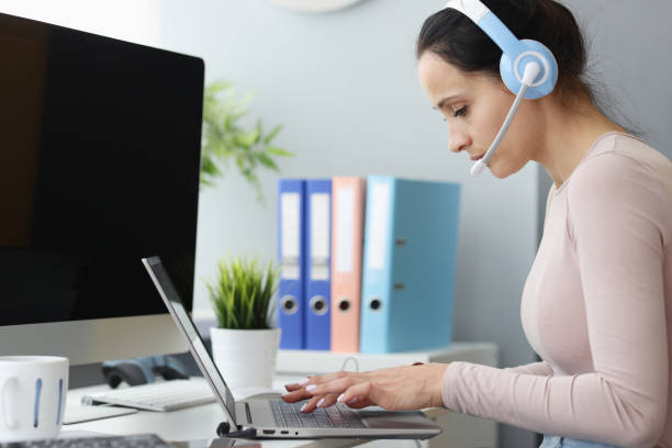istock Woman operator in headphones with microphone works at computer. 1436924724