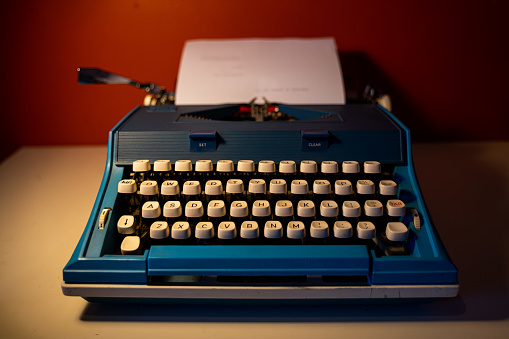 A photo of a vintage blue typewriter on a white table and an orange color wall