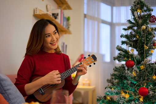 Woman is singing a Christmas song. She is playing ukulele. Christmas concept.