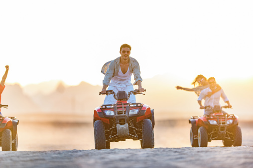 Young happy man and his friends having fun while driving quads in summer at the desert. Copy space.