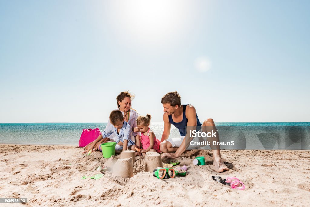 Young happy family playing with beach toys in sand. Happy parents and their small kids playing in sand on the beach. Copy space. Adult Stock Photo