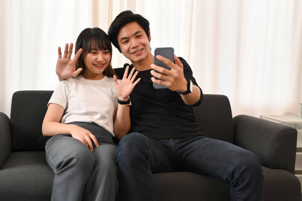 istock Happy young couple taking selfie, making video call on smart phone while sitting on couch at home. 1436929408