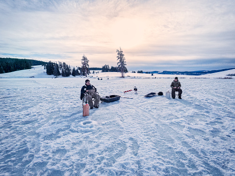 First Nations and Caucasian men in 60s and 70s ice fishing for rainbow trout at Marquart Lake, Merritt, British Columbia, Canada.