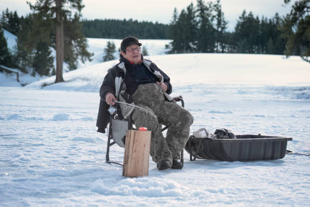 Indigenous Senior Man Ice Fishing on Frozen Lake First Nations man ice fishing for rainbow trout at Marquart Lake, Merritt, British Columbia, Canada. man ice fishing stock pictures, royalty-free photos & images