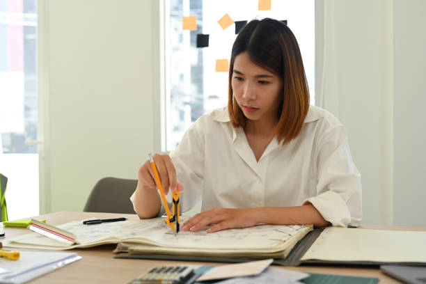 istock Concentrated young female architect working on blueprint at her workstation. 1436931755