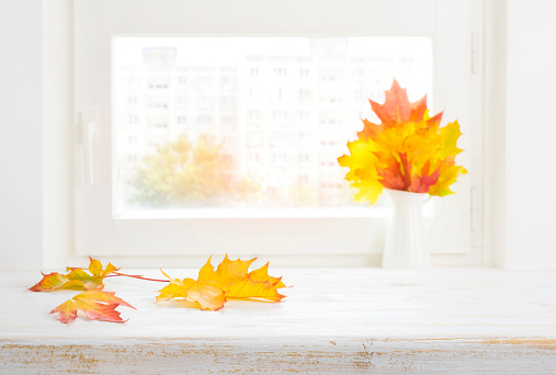 Autumn maple leaves on wooden table over blurred window background