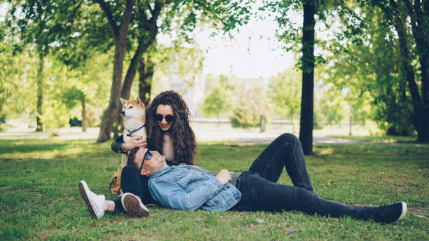 istock Handsome young man is lying on the grass in the park while his girlfriend is talking to him and petting cute dog, couple is laughing and enjoying weekend. 1436946154