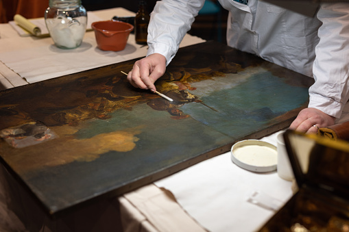 Experienced Lady Restoring an Antique Painting with a Special Wand.