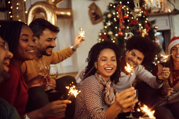 Multiracial group of happy friends using sparklers and having fun on New Year's day at home. Cheerful friends having fun with sparklers during Christmas party at home. new years eve parties stock pictures, royalty-free photos & images