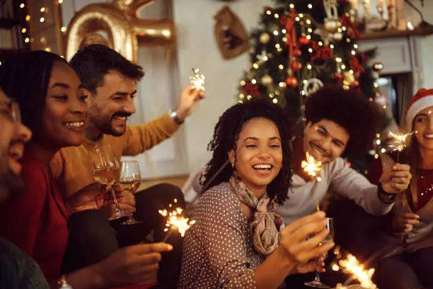 Photo of Multiracial group of happy friends using sparklers and having fun on New Year's day at home.