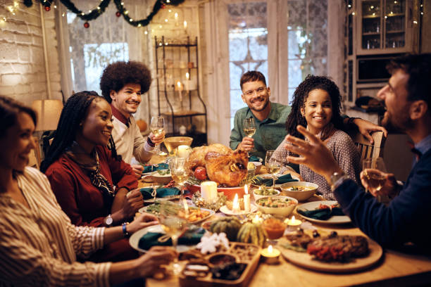 Young happy friends talking at dining table during Thanksgiving lunch. Multiracial group of friends drinking wine and communicating at dining during Thanksgiving meal. dinner party stock pictures, royalty-free photos & images