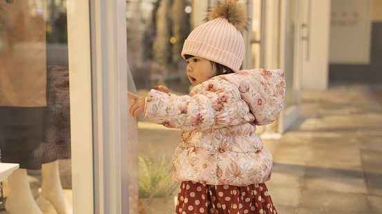innocent asian baby girl looking into the shop window with curiosity and eager to chase after something she spot outside a shopping mall in the winter