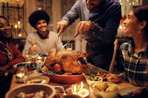 Close up of man carving roast turkey while having dinner with friends on Thanksgiving.