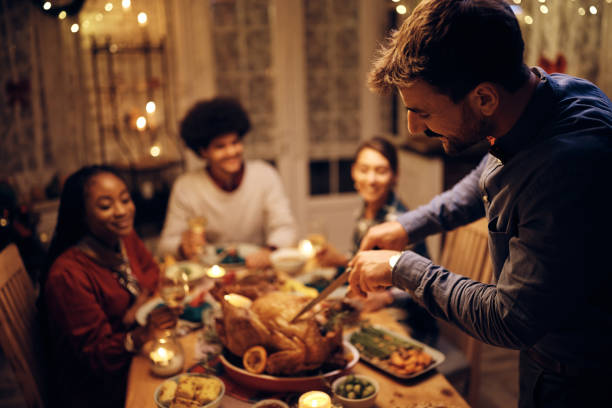istock Smiling man carving Thanksgiving turkey during dinner in dining room. 1436949602