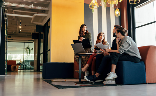 Business people working together in an office lobby. Group of young business people sitting together in an open plan co-working space. Team of creative entrepreneurs working in casual clothing.