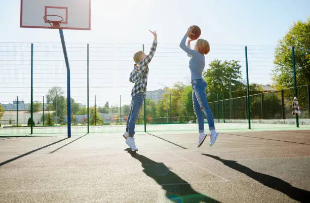 Group of teens, students playing street basketball at basketball court outdoors at spring sunny day. Sport, leisure activities, hobbies, team, friendship. Boys and girl spending time together.
