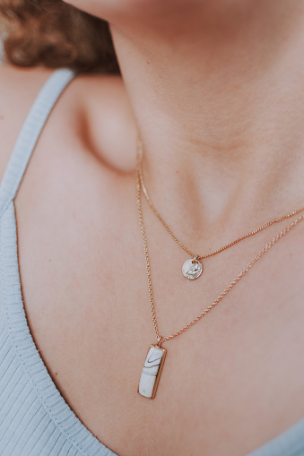A closeup of elegant necklaces with round and rectangular pendants on a female neck