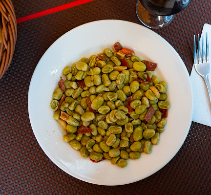 Habas with jamon on plate served with cutlery and glass of wine in restourant