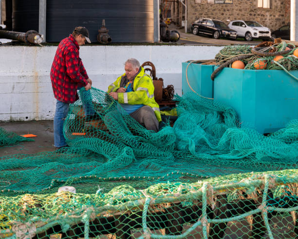 26 October 2022. Fraserburgh, Aberdeenshire, Scotland. This is two men in the process of repairing a large Fishing Net on the pier at Fraserburgh Harbour.