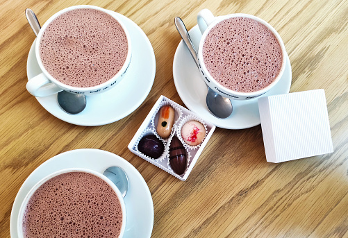 Three mugs of natural hot drink made from cocoa beans. Hot chocolate with milk and chocolates in a gift box.