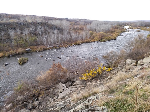 Rocky river bank among hills overgrown with vegetation, granite stones among dry yellowed grass