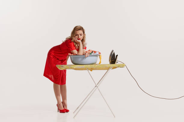 白い背景に洗濯後にアイロンをかける美しい女性のポートレート。イライラしている - 1950s style iron stereotypical housewife women ストックフォトと画像